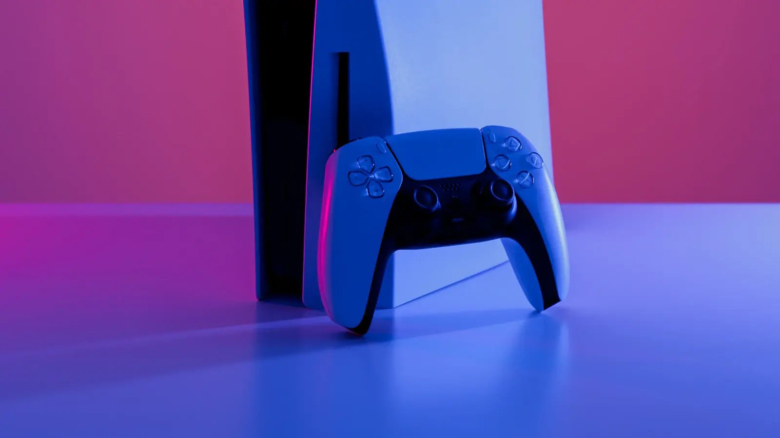 A white games console and controller lit by pink and blue studio lighting